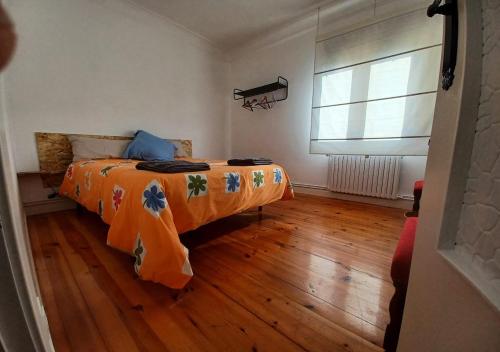 1 dormitorio con 1 cama con manta naranja y ventana en Habitaciones en El Atico de Tona mirando a la Bahia de Santander, en Santander