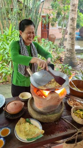 a woman is stirring a pot of food on a table at Ba Danh Homestay & Kitchen - Ben Tre Mekong in Ben Tre