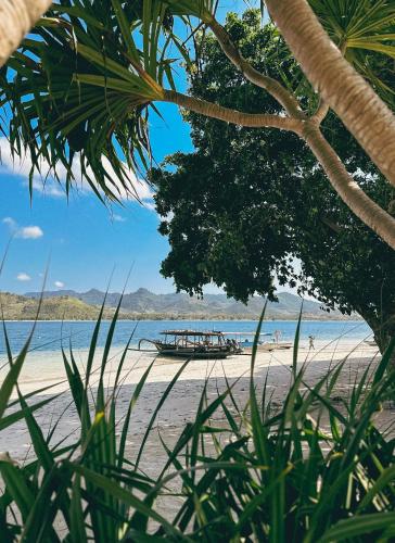 a boat sitting on a beach with a tree at Vayam Boutique Resort Gili Asahan in Gili Asahan