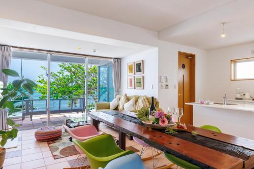 a living room with a wooden table and green chairs at 海まで徒歩1分 沖縄でも珍しい絶景ホテル 贅沢プライベートビーチ付き ビーチルーム in Onna