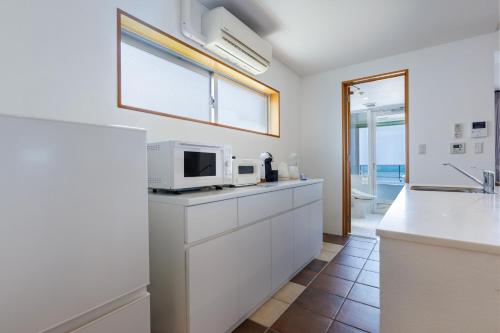 a kitchen with white cabinets and a microwave at 海まで徒歩1分 沖縄でも珍しい絶景ホテル 贅沢プライベートビーチ付き ビーチルーム in Onna