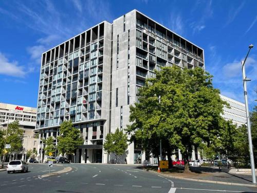 a large building with a tree in front of a street at Lovely CBD two bedroom apartment free parking gym and sauna in Canberra