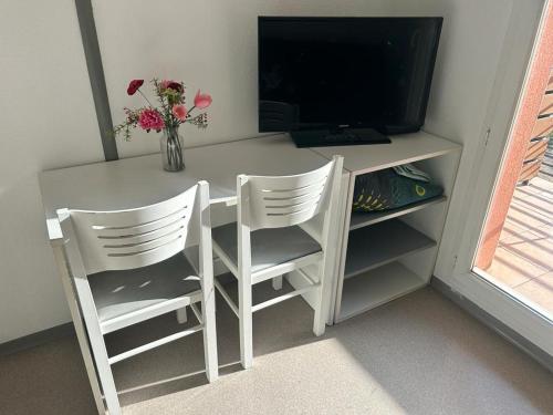 escritorio blanco con 2 sillas y TV en Studio residence de tourisme le Fonserane, en Béziers