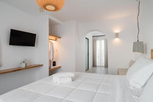a white bedroom with a large white bed and a television at Castello studios in Agia Anna Naxos