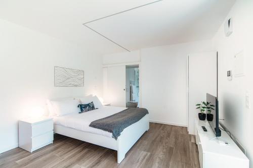 a white bedroom with a bed and a tv at La Palma 3 by Quokka 360 - studio with terrace and lake view in Montagnola