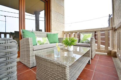 patio con sillas de mimbre y mesa en el balcón en Luxury Dreams in Playa Paxariñas, en Sanxenxo