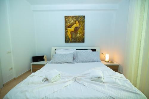 a bedroom with a white bed with a painting on the wall at Hana apartament hot tub in Vlorë