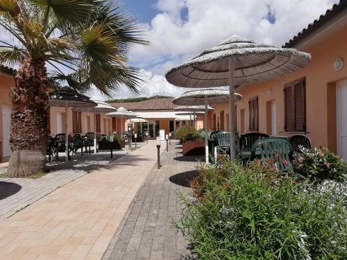 un patio con mesas, sillas y una sombrilla en Hotel Le Palme, en Albinia