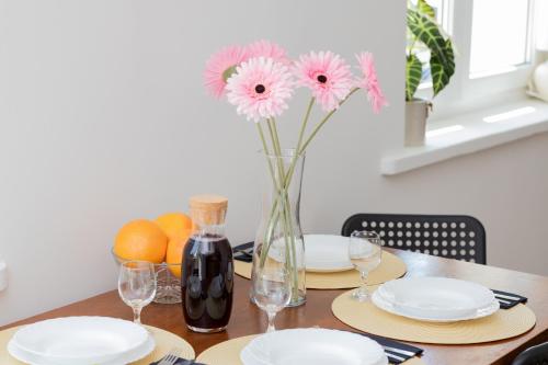 a table with plates and a vase with pink flowers at Gdynia City Centre Apartment Abrahama by Renters in Gdynia