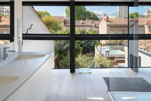 une cuisine avec comptoirs blancs et une grande fenêtre dans l'établissement Maison contemporaine plein centre piscine &jacuzzi, à Toulouse