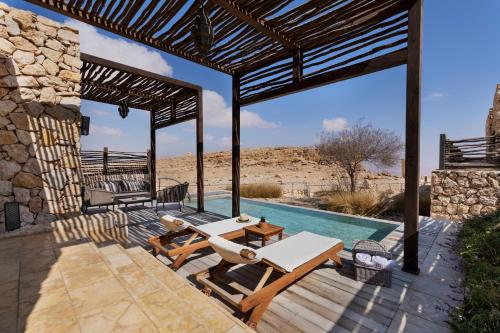 an outdoor patio with a table and chairs and a pool at Beresheet by Isrotel Exclusive in Mitzpe Ramon