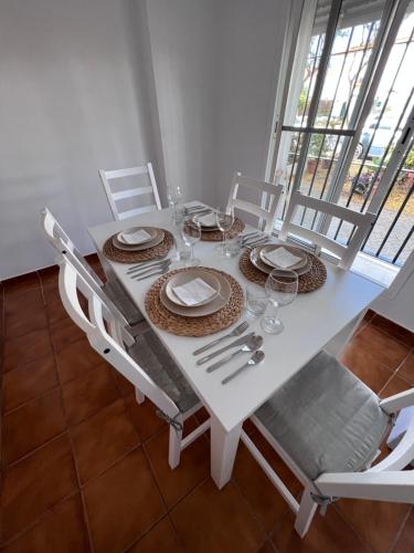 una mesa de comedor blanca con sillas blancas, platos y vasos en Casa de Fernando, en Puerto Real