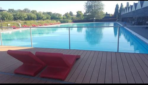 une grande piscine avec des chaises rouges sur une terrasse en bois dans l'établissement Au chant des oiseaux, à Rochefort