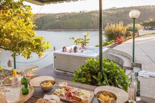 two people in a bathtub on a deck next to the water at Castelo de Bode - Lake House, A Casa do Avô in Levegada
