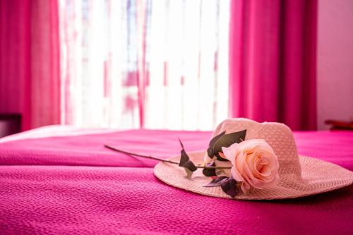 a hat with a flower on a pink bed at Hotel Oasis Atalaya in Conil de la Frontera