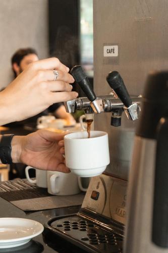 a person is preparing a cup of coffee in a kitchen at Raf Hotel in Umuarama
