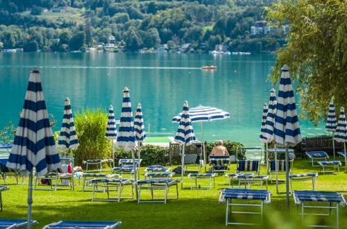 a group of lawn chairs and umbrellas in front of a lake at Strandhotel Habich in Krumpendorf am Wörthersee