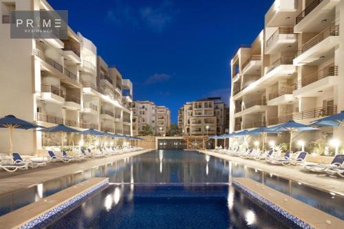 a swimming pool with chairs and umbrellas in front of buildings at Marina Residence New Alamein 2 bedroom apartment in El Alamein