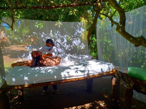 a woman sitting on a bed under a tree at Cabañas Los Venaos in San Bernardo del Viento
