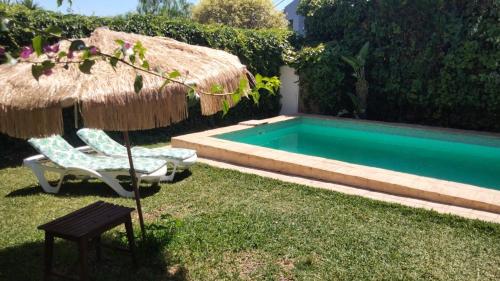 a pool with a straw umbrella and a chair and a table at Dormir entre limones, Casa de invitados en vivienda familiar in Dos Hermanas