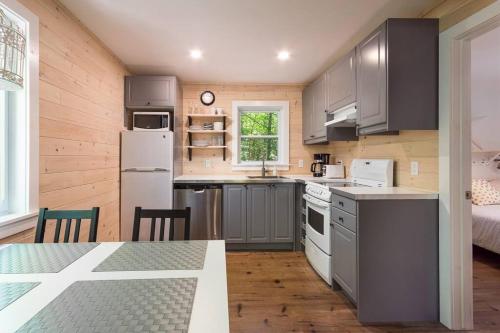 a kitchen with gray cabinets and a table and a bed at Oasis de paix sous les arbres, avec accès au quai, à 1h de Montréal in Saint-Calixte