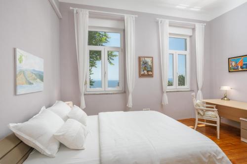 a white bedroom with a bed and a desk and windows at Apartment Gloria in Opatija