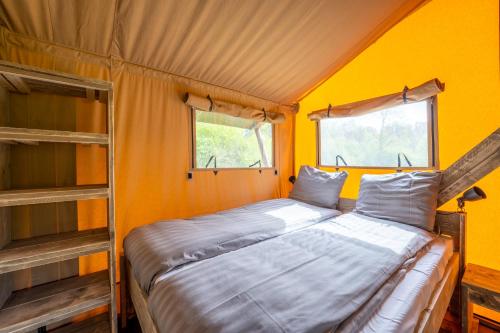 łóżko w pokoju z żółtymi ścianami i dwoma oknami w obiekcie Sunny Trio w mieście Zeewolde