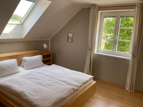 a bedroom with a bed with white sheets and two windows at Chalupa u Pavelků 