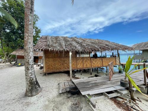 eine Hütte am Strand mit einer Bank und einem Baum in der Unterkunft Kri guest homestay in Rancakole