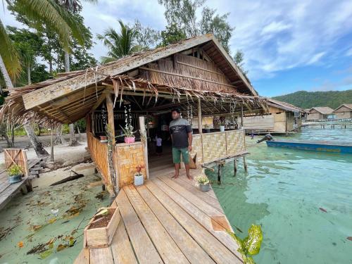 a man standing outside of a house on the water at Kri guest homestay in Rancakole