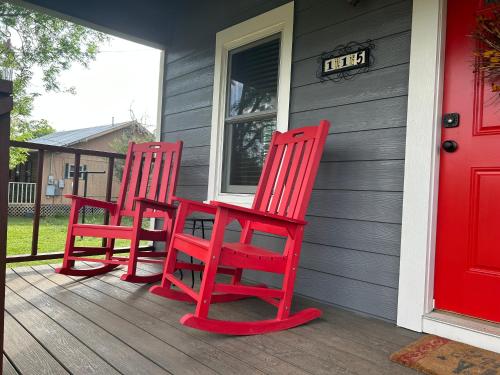 two red chairs sitting on the front porch of a house at Bandera Bungalow - River, Downtown, Peaceful fenced corner lot! King bed! in Bandera
