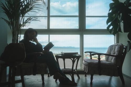 a woman sitting in a chair with a laptop in front of a window at Hotel 2YL Atami in Atami