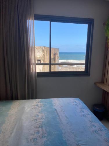 een slaapkamer met een raam met uitzicht op de oceaan bij Estúdio com Decoração Charmosa e Piscina compart in Salvador