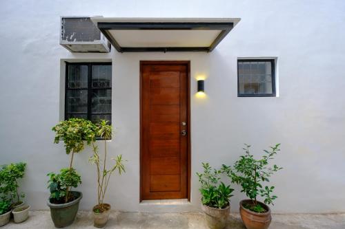 uma casa branca com uma porta de madeira e vasos de plantas em The House of Windsor - QC em Manila