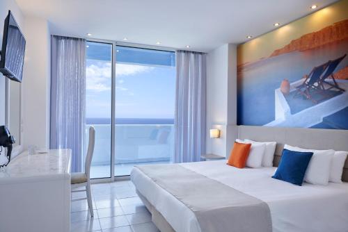 um quarto de hotel com uma cama, uma secretária e uma grande janela em Epsilon Hotel Apartments em Faliraki
