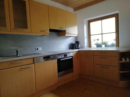 d'une cuisine avec des placards en bois, une cuisinière et une fenêtre. dans l'établissement Ferienwohnung Hinterschwarzenberg, à Brixlegg