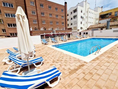 a pool with chairs and umbrellas next to a building at Hotel Santa Cecilia in Ciudad Real