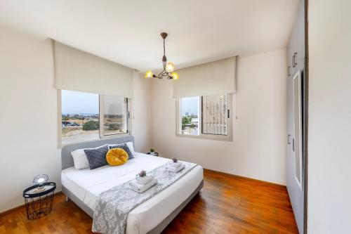 une chambre avec un grand lit blanc et deux fenêtres dans l'établissement Mackenzie Beachfront Eftyhia Suite, à Larnaka