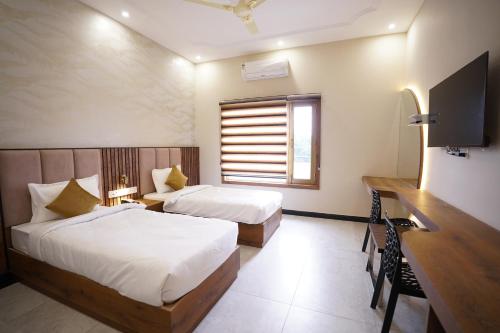 a bedroom with two beds and a desk and a television at Dreamy Desert Hotel in Haldwāni