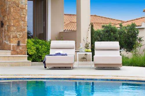 two lounge chairs sitting next to a swimming pool at Ajul Luxury Hotel & Spa Resort, a Registry Collection Hotel in Agia Paraskevi