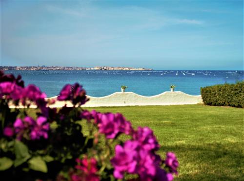 a view of the beach with pink flowers in the foreground at Villa Incanto on the Sea in Siracusa