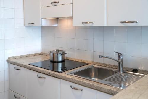 una cocina con fregadero de acero inoxidable y armarios blancos en Residence Casa al Sole Apartments, en Nago-Torbole