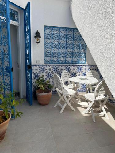 un patio con sillas blancas, una mesa y azulejos azules en Dar El HABIB, en Douar el Hafey
