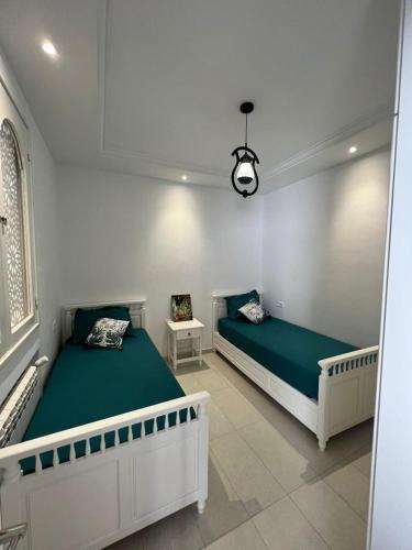 2 bedden in een witte kamer met groene lakens bij Dar El HABIB in Douar el Hafey