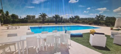 una piscina con sillas blancas, una mesa y una piscina en B&B Uliveto, en Cerignola