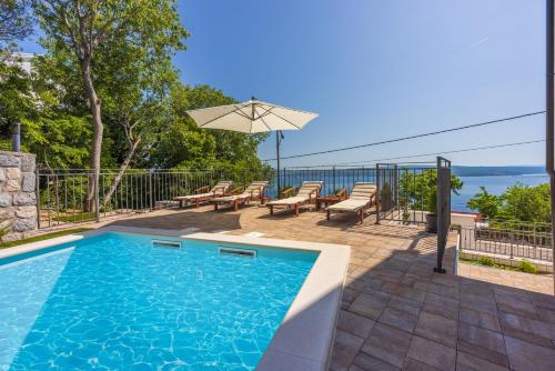a swimming pool with chairs and an umbrella on a patio at Villa Antani with heated pool, sauna & jacuzzi in Crikvenica