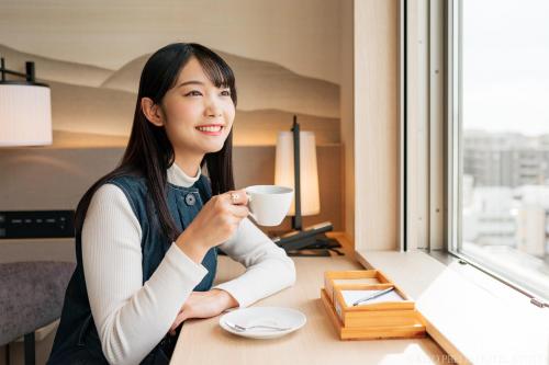 una mujer sentada en un escritorio con una taza de café en Keio Prelia Hotel Kyoto Karasuma-Gojo, en Kioto