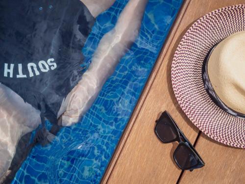 a pair of sunglasses and a hat next to a swimming pool at ARCELON HOTEL - From 2023 in Barcelona