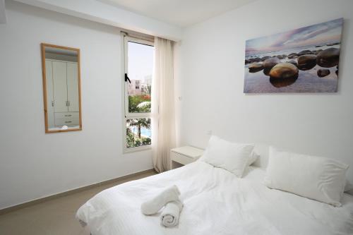 a white bedroom with a large white bed and a window at Golf Residence Sea and Soul in Eilat