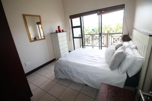 a bedroom with a bed with white pillows and a balcony at Topanga 70, Uvongo in Margate